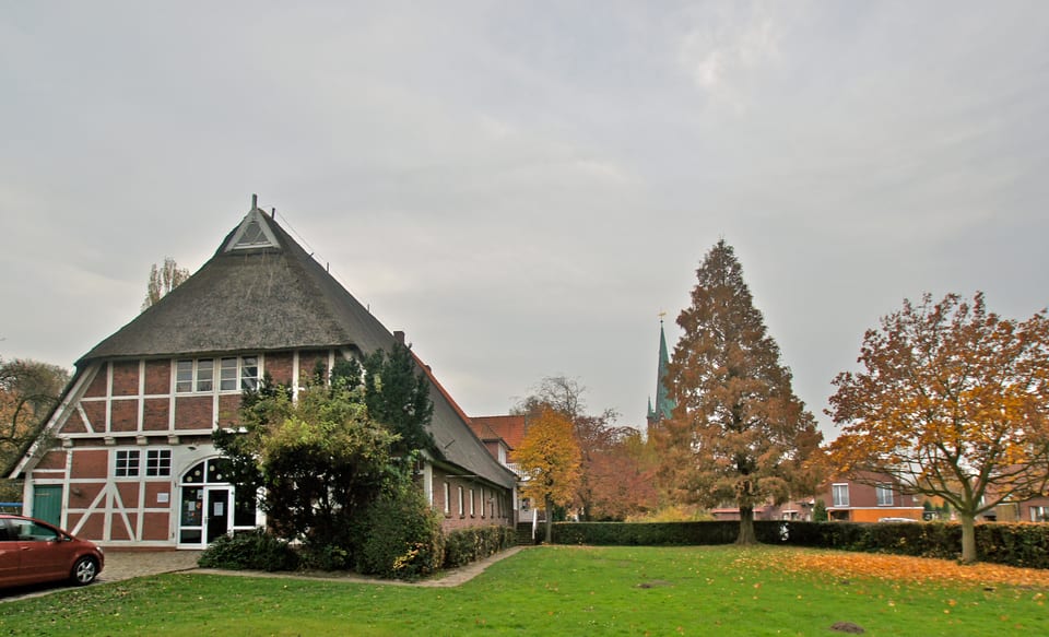Reetgedecktes Fachwerk-Pastorat von St. Nikolai am Moorfleeter Kirchenweg mit dem Kirchturm im Hintergrund